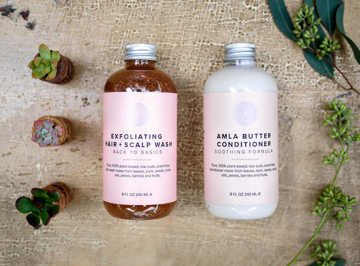 two product bottles with pink labels placed side by side and surrounded by greenery 