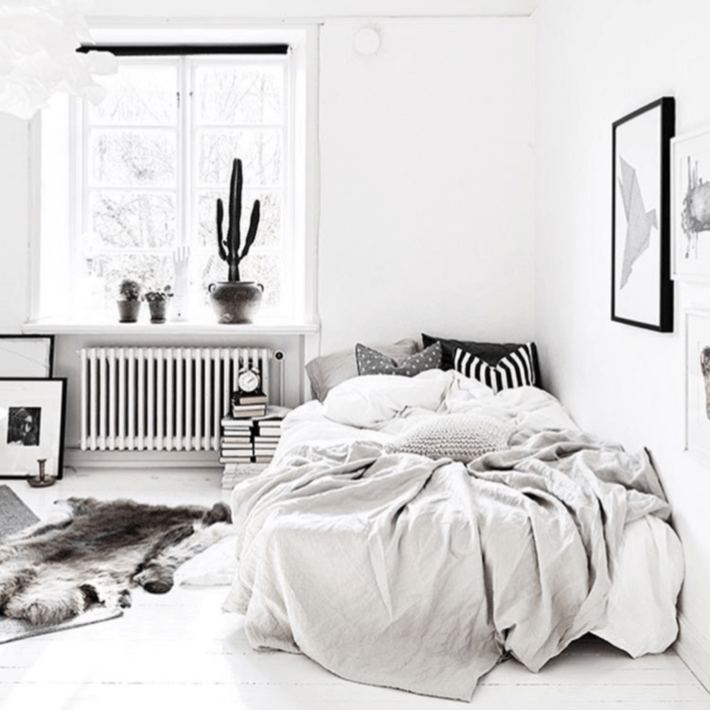 a black and white photo of a room styled with a cactus and tons of sheets and blankets on the bed 