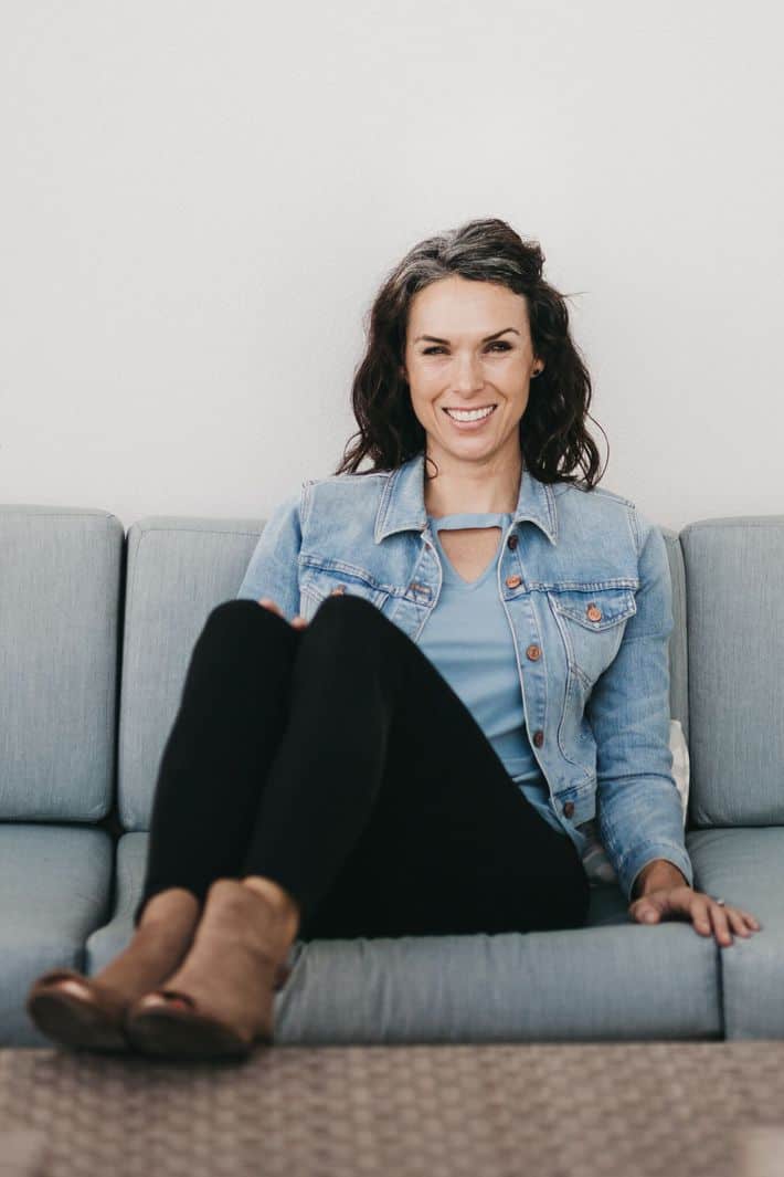 a woman sitting on a couch wearing a jean jacket and black jeans 