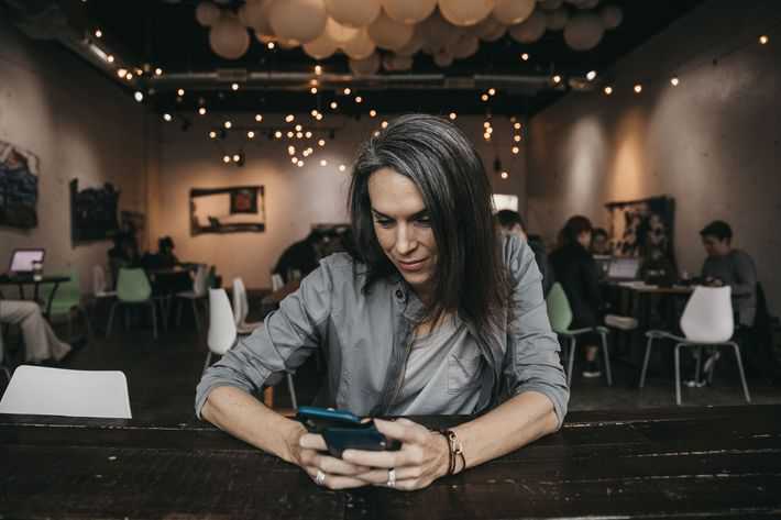 forty year old woman sitting in a coffee shop looking down at smartphone with the lighting showing her gray hair