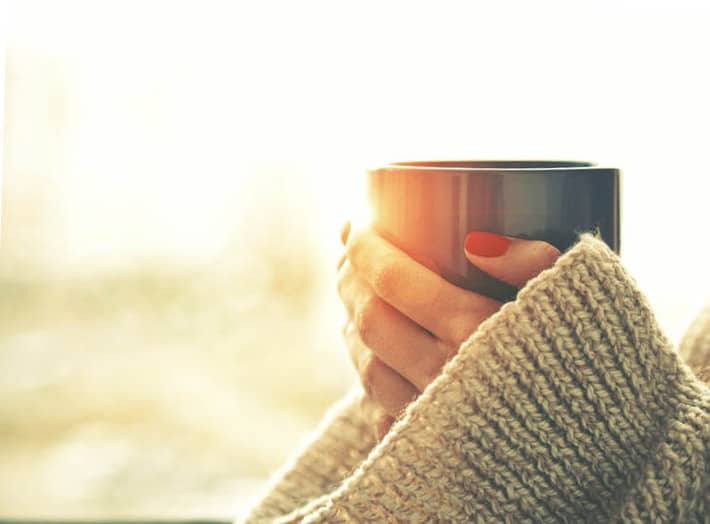holding a cup of coffee wearing a big sweater and adorning red nails