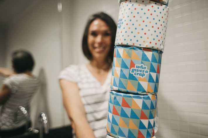 a woman holding up several rolls of toilet paper stacked vertically in a bathroom