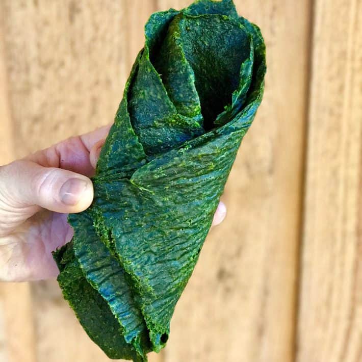 holding a sheet of green raw veggie bread folded over on itself 