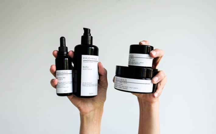 holding KHUS + KHUS organic skincare up in two hands against a gray background