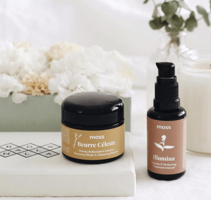 two moss skincare products styled with flowers and a candle 