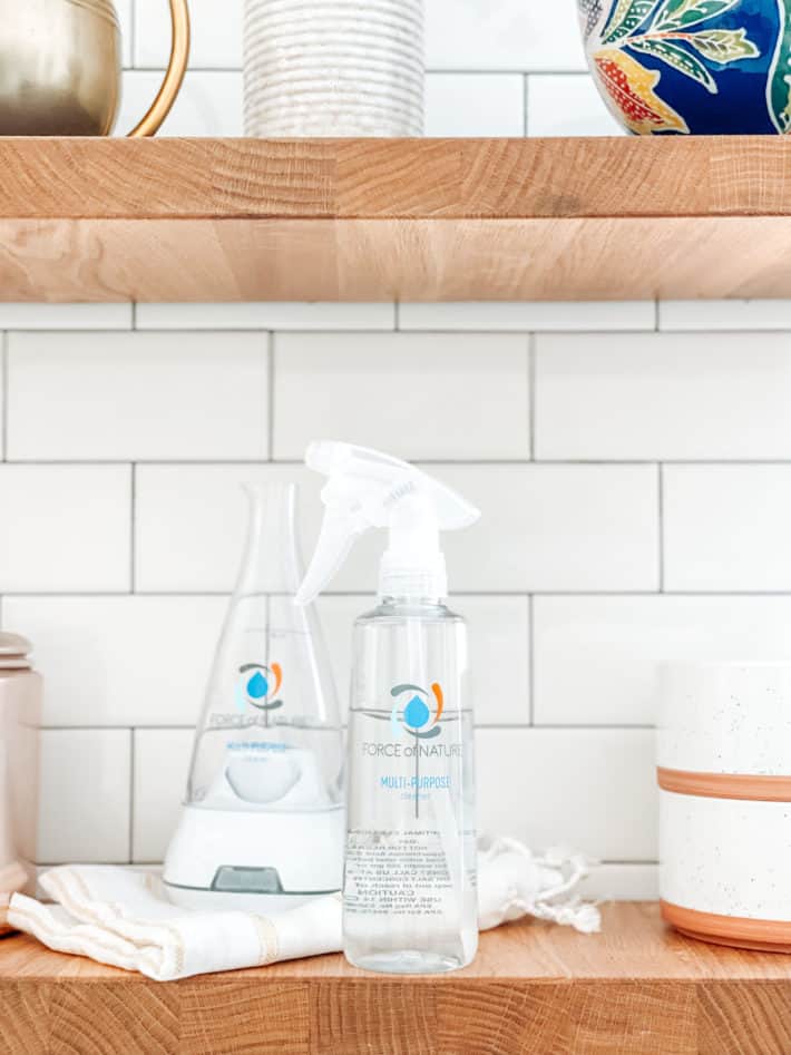 A clear spray bottle sits on a butcher block shelf next to terracotta bowls