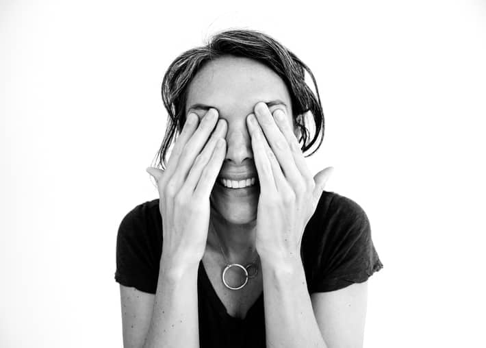 black and white photo of woman smiling and covering her eyes 