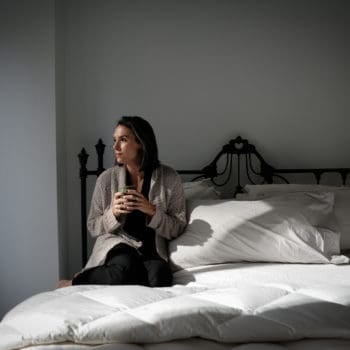 a woman sitting on her bed drinking a warm drink