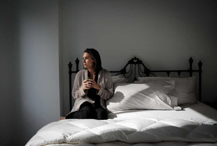 a woman sitting on her bed drinking a warm drink