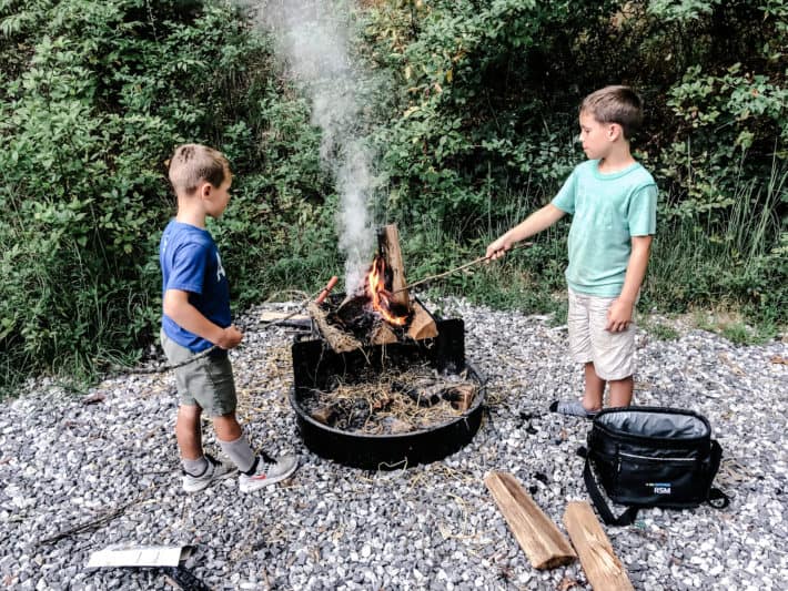 kids cooking hotdogs over an open fire in the woods
