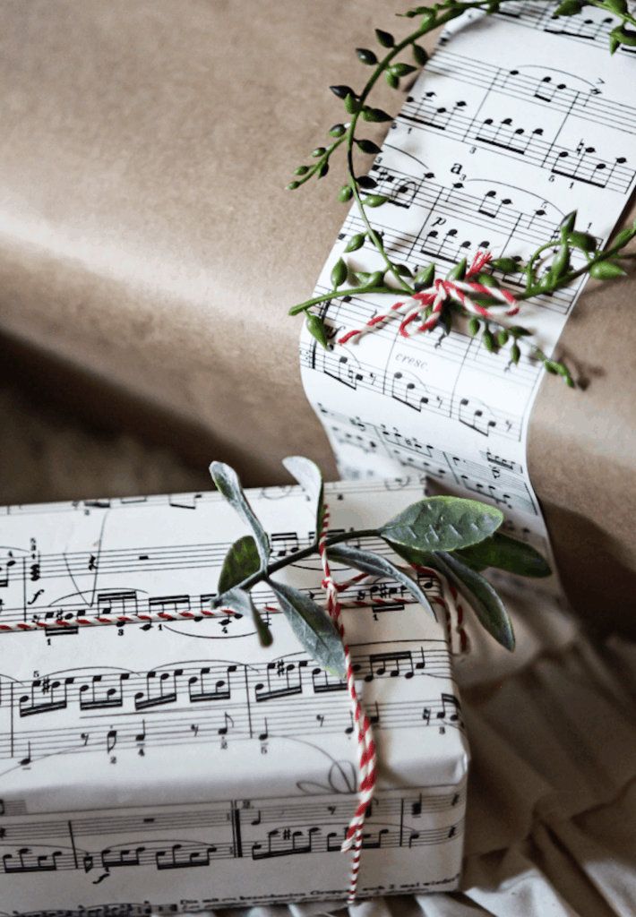 two gifts wrapped in sheet music with berries and greenery