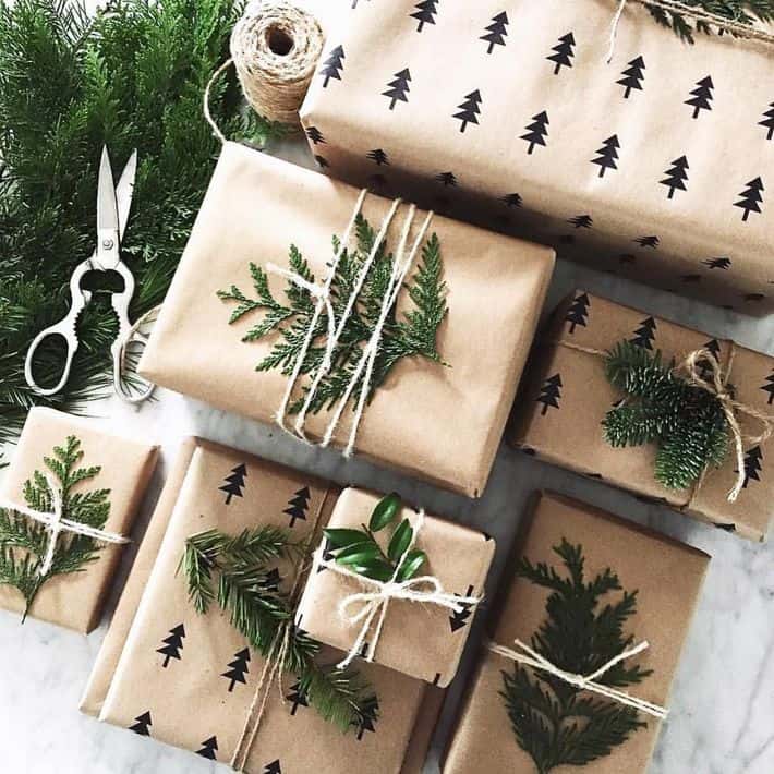 several gifts wrapped in brown paper, twine, foliage and stamped pine trees