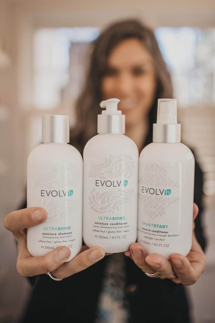Lisa holding three bottles of EVOLVh haircare products