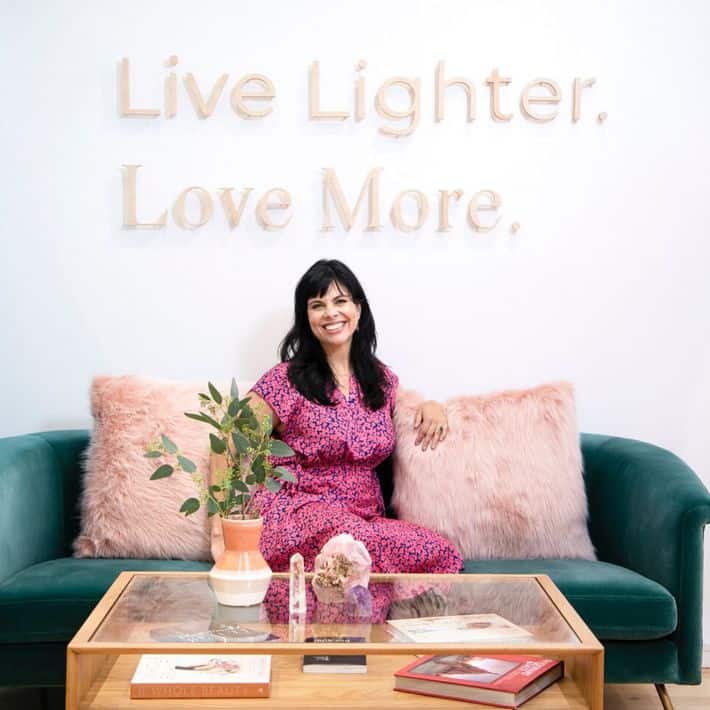 Jeannie sitting on a green couch with wall decor behind her reading "Live Lighter. Love More."