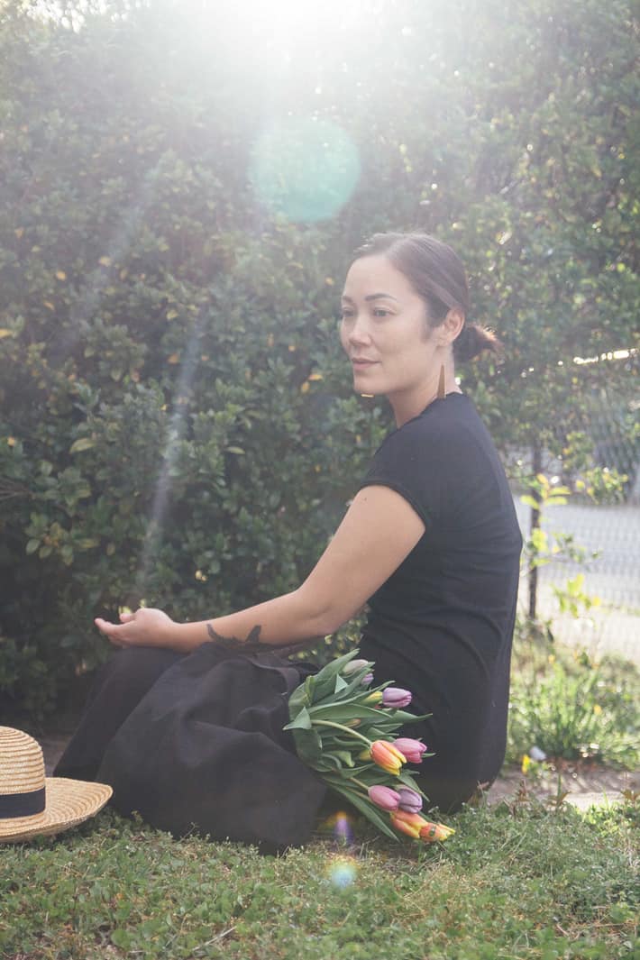 Tanya sitting in her yard while wearing a black maxi dress with a bouquet of flowers next to her.