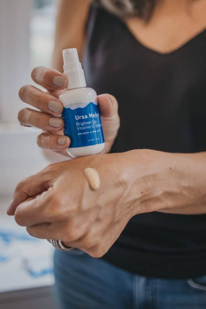 One hand holding bottle of brightening serum with sample of serum displayed on other hand