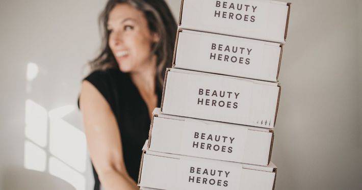 A woman holds up a stack of beauty heroes boxes.