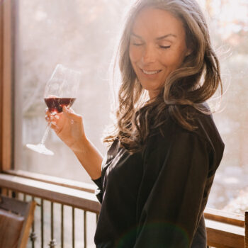 A woman stands on a porch holding a glass of dry farm wines wine.