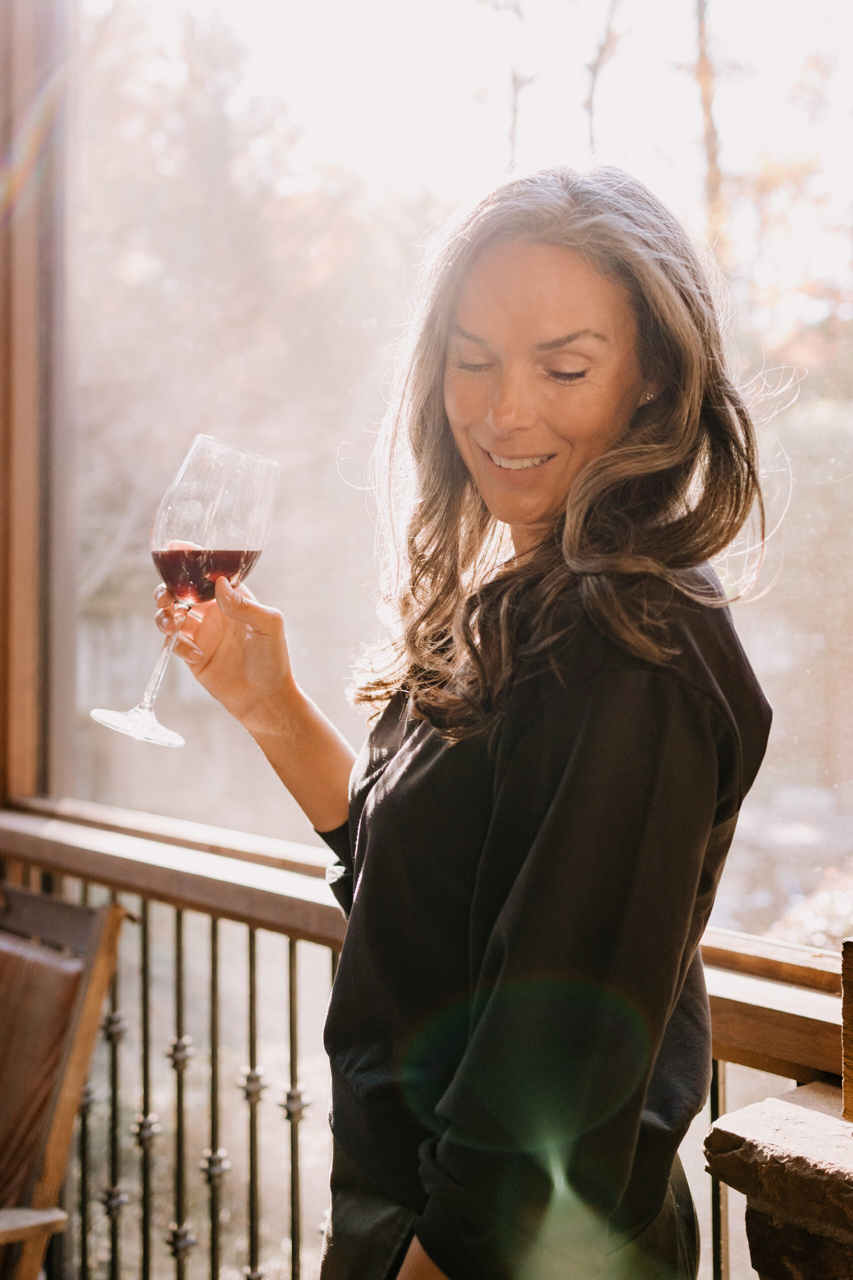 A woman stands on a porch holding a glass of dry farm wines wine.
