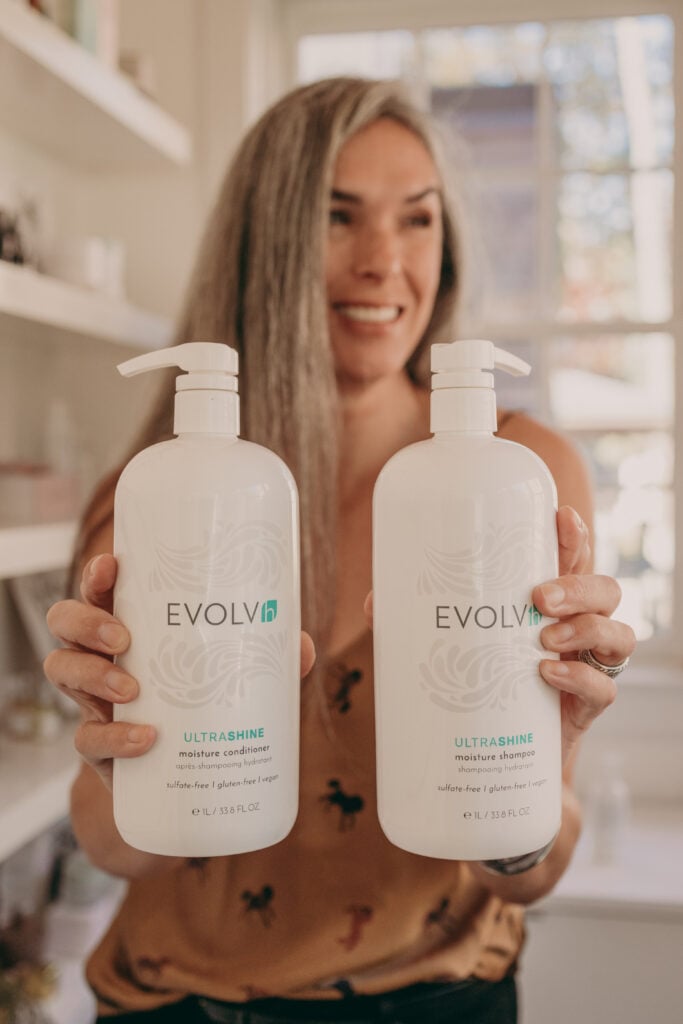 A woman holds up a shampoo liter bottle from EVOLVh