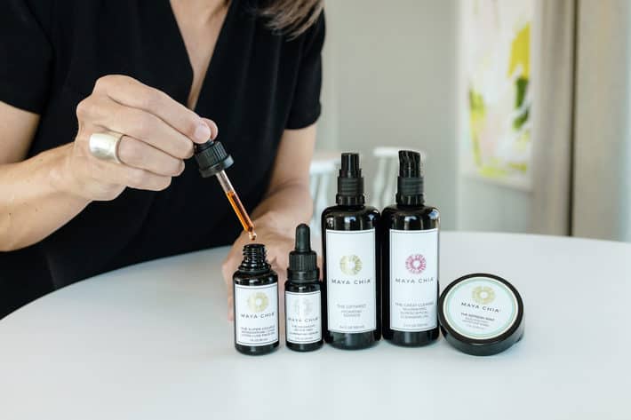 Maya Chia skincare lined up on a table with Lisa holding a dropper