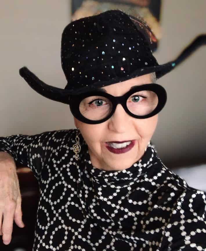 Woman with gray hair wearing a hat and fabulous glasses