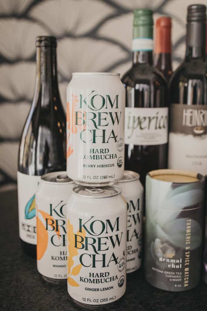 Cans of Kombrewcha stacked in front of wine bottles
