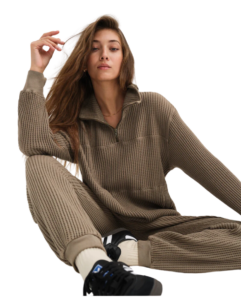 A woman sits in a waffle sweatshirt and joggers.