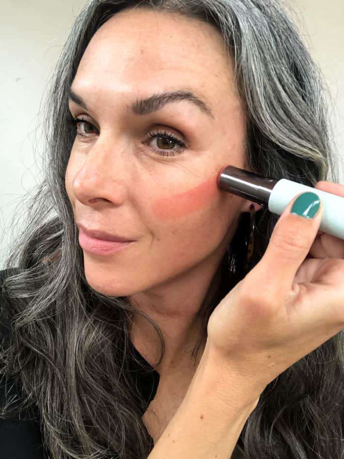 applying coral vapour multi-stick to light-skinned cheek