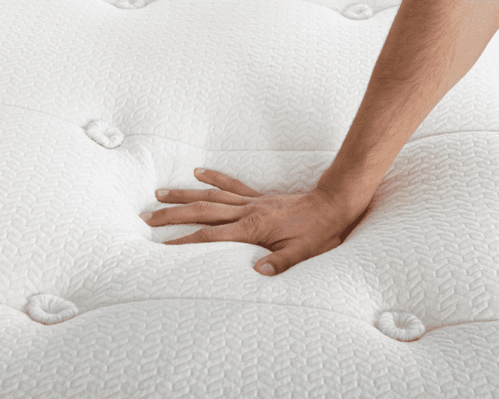 A hand presses gently on a latex-free mattress.