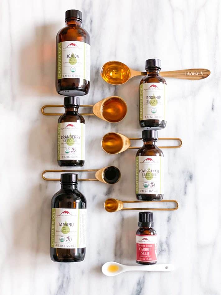 Bottles of facial oils lay on a marble stone next to gold measuring spoons.