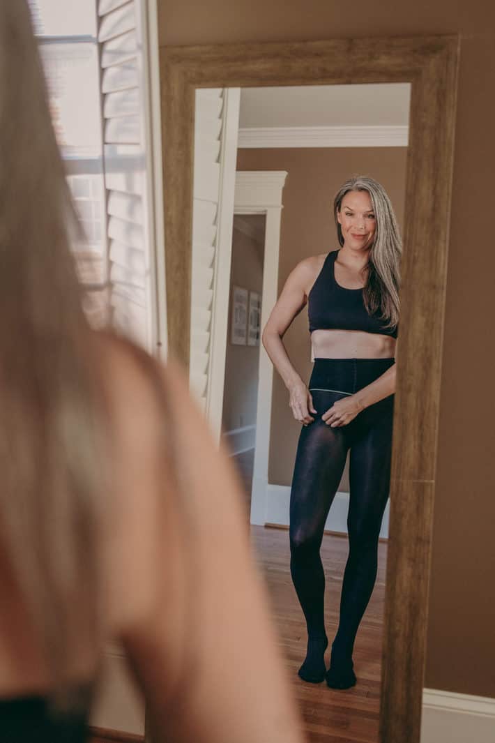 Lisa stands in front of a mirror looking at her shaping tights.