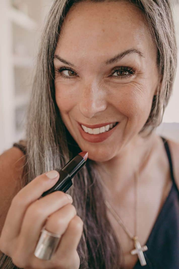 woman smiling and applying lipstick