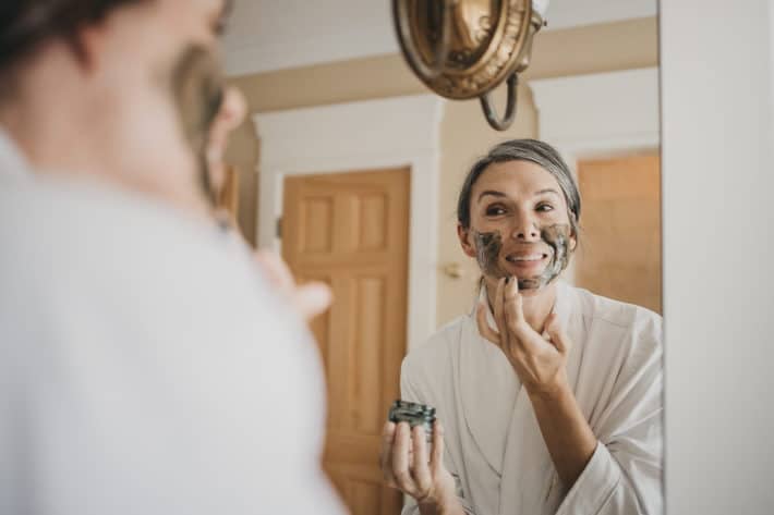 Lisa applies a green, honey-based face mask while looking in the mirror.