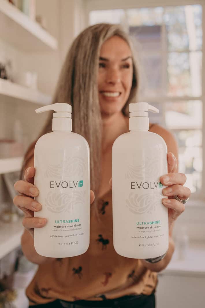 lisa holds out liter bottles of clean shampoo and conditioner from EVOVLh