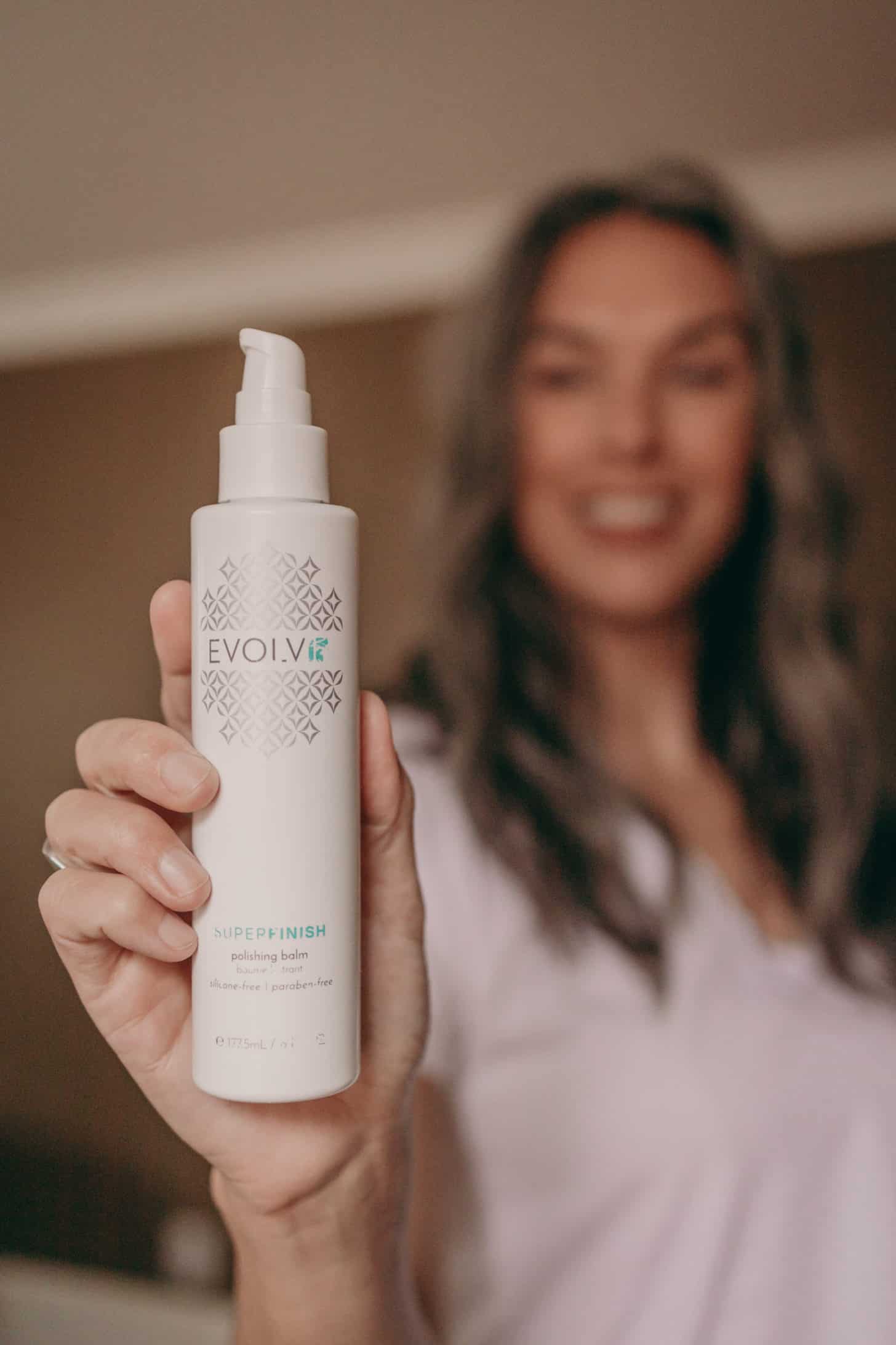 a woman holds out a bottle of heat protectant super finish polishing balm from evolvh haircare