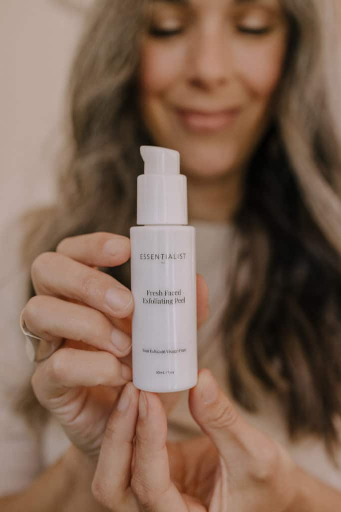 A woman holding up a bottle of Essentialist face oil.