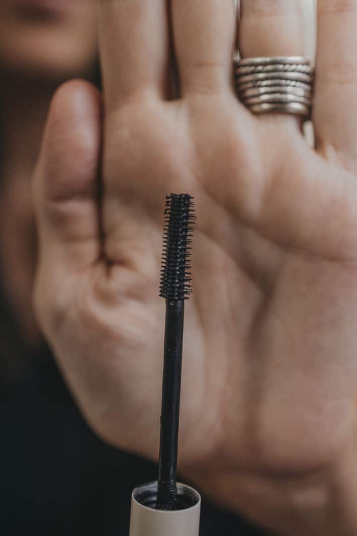 A mascara wand is held in front of a hand.