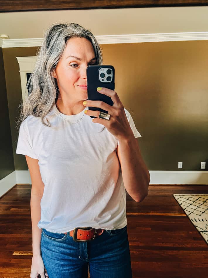A woman wears a white tshirt taking a selfie in the mirror.