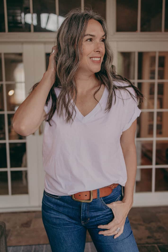 A woman wearing a white t shirt and jeans smiles while looking off to the side