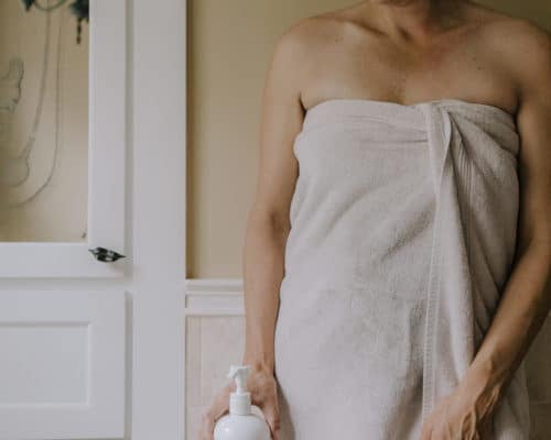 a woman stands near a bathtub holding a bottle of shampoo