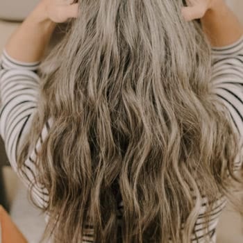 the back of a woman's head who has long gray hair extensions