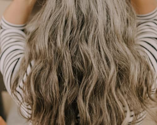 the back of a woman's head who has long gray hair extensions