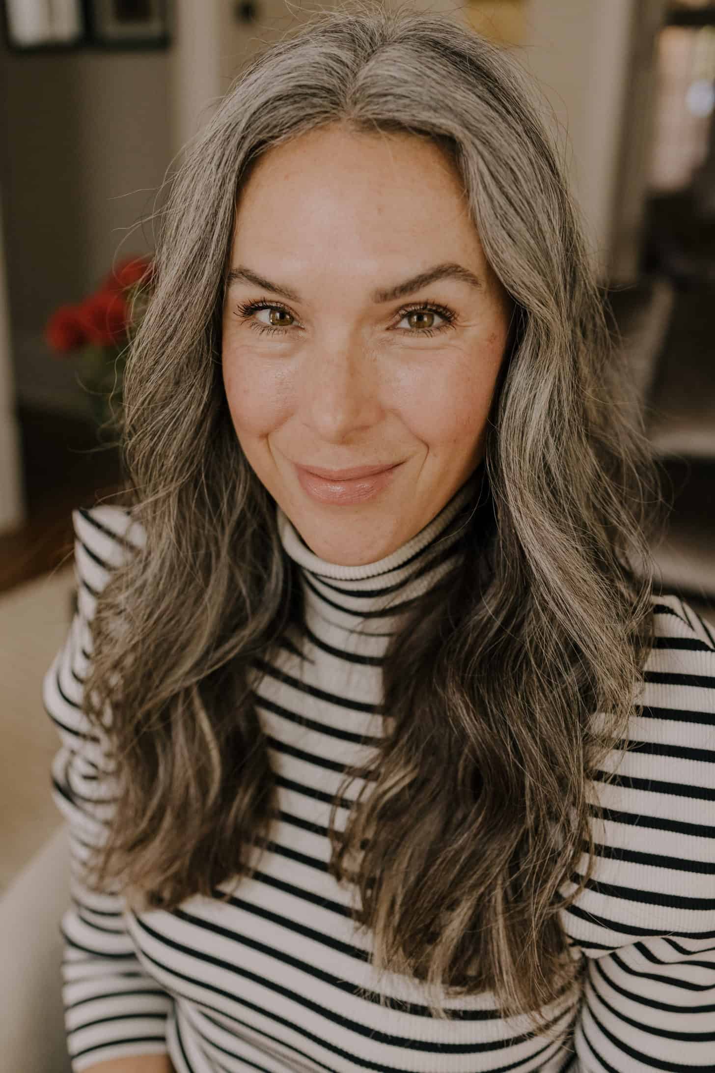 a smiling woman with long gray hair extensions in a black and white striped shirt