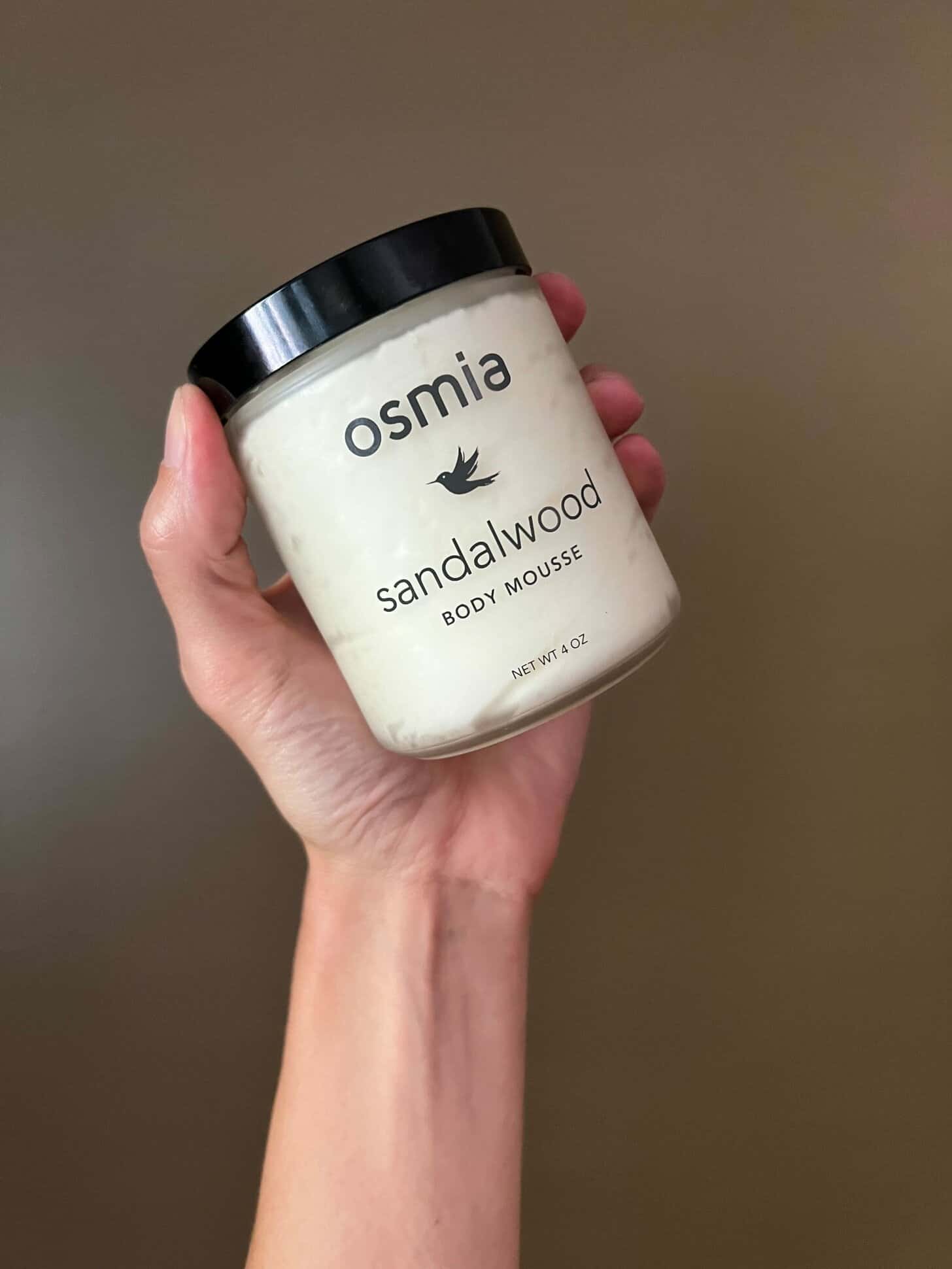a container of osmia sandalwood body mousse is held in someone's hand