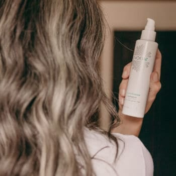 a woman with wavy long gray hair looks at a bottle of evolvh spray
