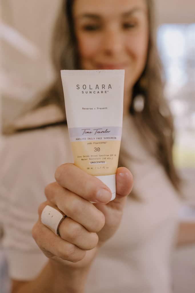a woman holding up a bottle of solara suncare time traveler