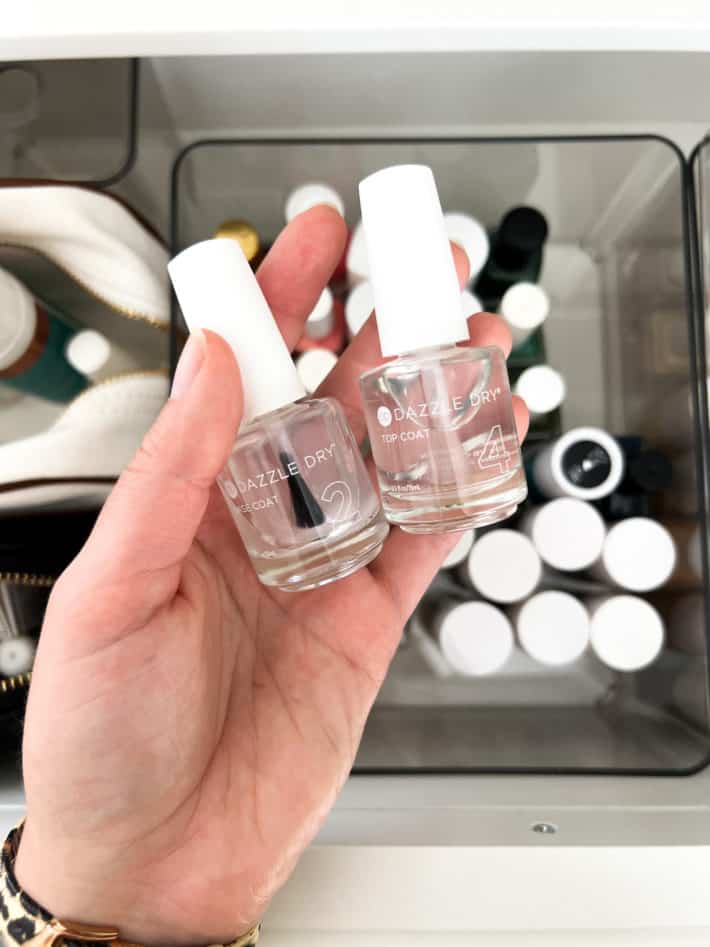 a close up of a hand holding dazzle dry brand base and top coats for fingernails