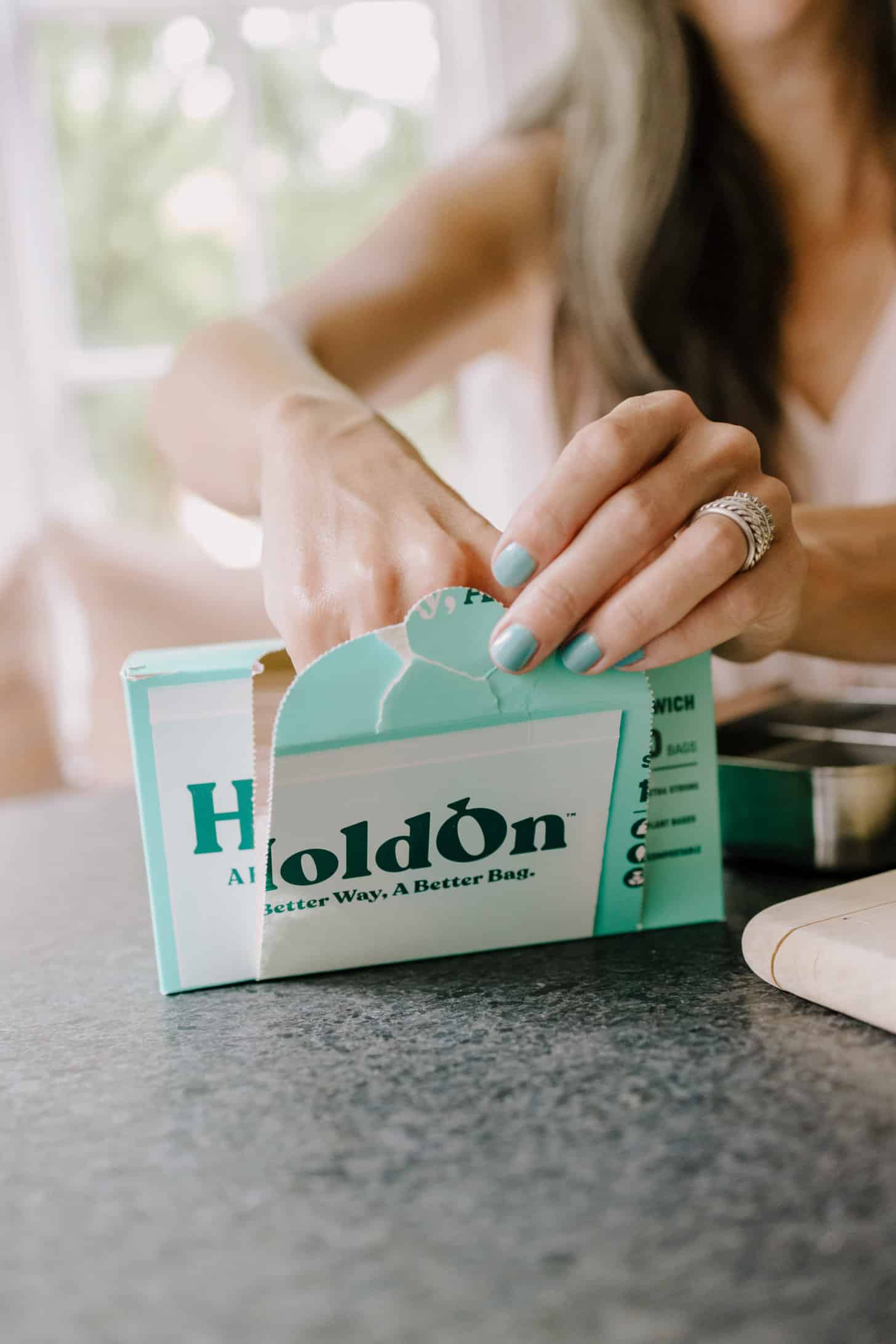 a woman with painted fingernails opens a box of HoldOn compostable bags