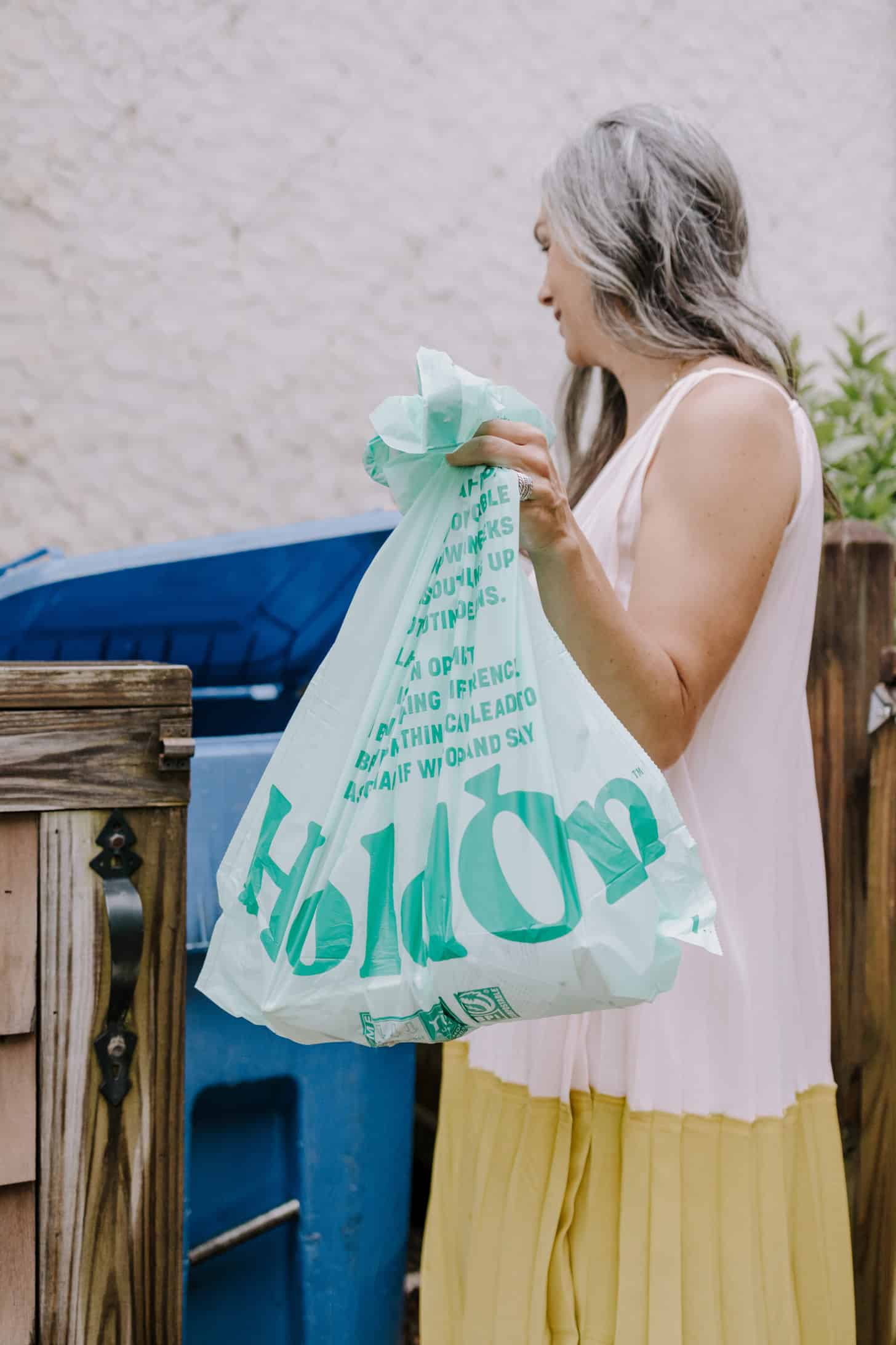 a woman holds a large HoldOn compostable trash bag as she lifts the lid to a garbage can